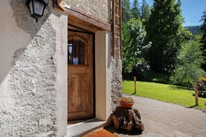 Un edificio rustico con una porta in legno, un lanternino e uno sgabello di legno decorato con fiori.