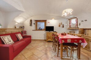 A cozy interior with a red sofa, wooden dining table, and a TV on a wooden cabinet. - Apartment 'Lo Baou' with Shared Terrace, Shared Garden and Wi-Fi (Charvensod)