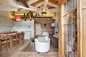 Een rustiek interieur met zichtbare houten balken, een eethoek met houten stoelen, een bank en een open haard.