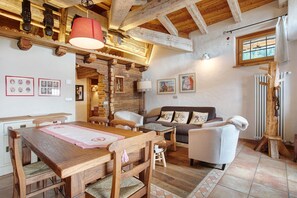 A wooden dining table with chairs, a sofa, and a wooden ceiling with exposed beams.