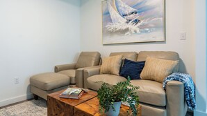 Ett vardagsrum med en beige soffa, ett soffbord med en växt och en tavla på väggen.
