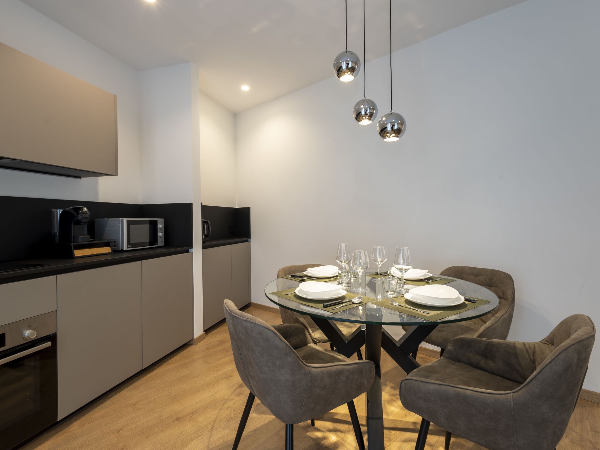 Una cucina moderna con zona pranzo. Include un forno a microonde, una macchina per il caffè e un tavolo da pranzo apparecchiato con piatti e bicchieri.