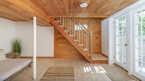 A wooden interior with a staircase, a sofa, and a large window.