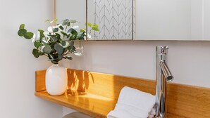 A bathroom with a wooden vanity, a white sink, a mirror, and a potted plant.