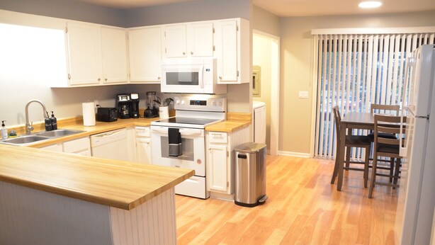 A modern kitchen with white cabinets, a stainless steel trash can, and a wooden dining table with chairs.