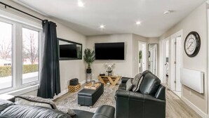 Uma sala de estar moderna com um sofá de couro preto, uma mesa de centro e uma televisão de tela plana na parede.