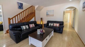 A living room with two black leather sofas, a wooden staircase, and a hallway leading to another room. - Family-Friendly Oasis with Pool, Near Beaches & Theme Parks (Ashmore)