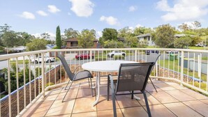 A balcony with a round table and two chairs, overlooking a street with parked cars and houses. - Family-Friendly Oasis with Pool, Near Beaches & Theme Parks (Ashmore)