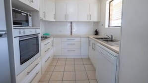 A compact kitchen with white cabinets, a built-in oven, a dishwasher, and a window providing natural light. - Family-Friendly Oasis with Pool, Near Beaches & Theme Parks (Ashmore)