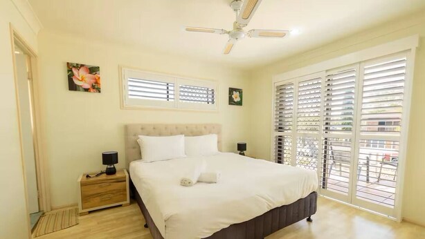 A bedroom with a bed, nightstands, a ceiling fan, and large windows with blinds. - Family-Friendly Oasis with Pool, Near Beaches & Theme Parks (Ashmore)