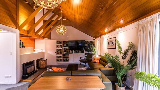 A modern living room with a wooden ceiling, a fireplace, a TV, a sofa, and a dining table. - Epic Games Room | 3-min to Hot Pools | Pets OK (Hanmer Springs)