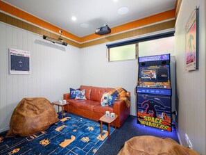 A room with a couch, bean bag, arcade games, a projector, and a poster.