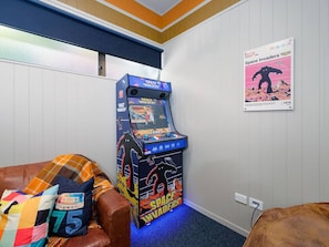A room with a Space Invaders arcade game, a couch with a colorful blanket, and a poster on the wall.