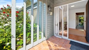 A covered outdoor area with a glass door leading to a patio, surrounded by plants and flowers. - Epic Games Room | 3-min to Hot Pools | Pets OK (Hanmer Springs)