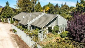 A two-story house with a sloped roof, satellite dish, and a fenced yard with various plants. - Epic Games Room | 3-min to Hot Pools | Pets OK (Hanmer Springs)