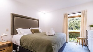 A bedroom with a bed, bedside table, lamp, and a view of greenery through the window. - Epic Games Room | 3-min to Hot Pools | Pets OK (Hanmer Springs)