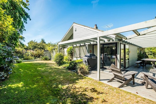 A covered patio with a grill, outdoor seating, and a view of a lush garden.