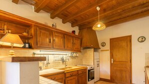 A kitchen with wooden cabinets, a stove, a sink, and a hanging light fixture. - Les 2 plages by Interhome (Vaux Sur Mer)