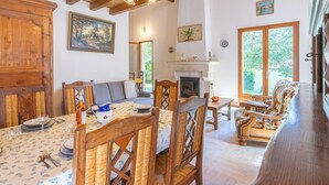A spacious living room with a fireplace, wooden furniture, and a dining area with a table set for four. - Les 2 plages by Interhome (Vaux Sur Mer)