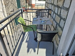 A small outdoor balcony with a table and chairs, a stone wall, and a metal railing.