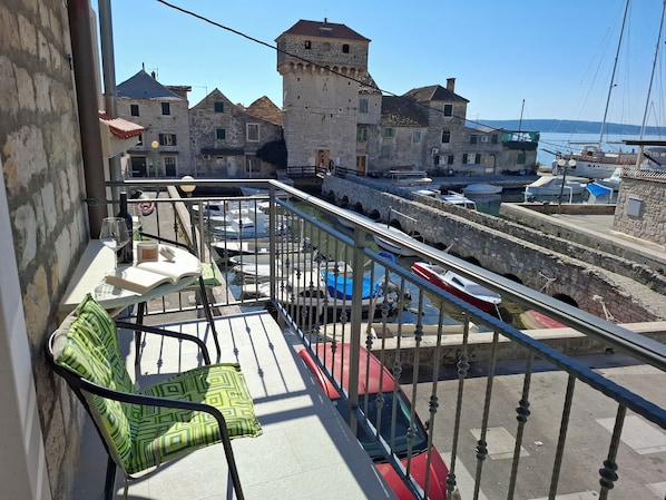 A balcony with a view of a historic stone building and a marina with boats.
