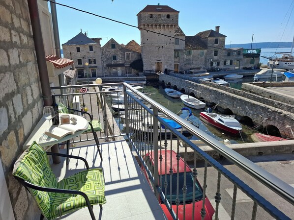 A balcony with a view of a historic town, stone buildings, and a marina with boats.