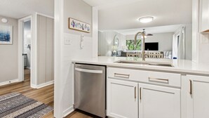 A modern kitchen with white cabinetry, a stainless steel dishwasher, and a central island with a sink. - Coastal Oasis: Just Steps to Beach, Shared Pool, Dining (Amelia Island)