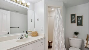 Ein Badezimmer mit weißem Waschbecken, Spiegel und Toilette. An der Wand befinden sich Bilder in Rahmen und ein Duschvorhang.