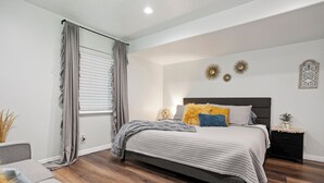 Ein Schlafzimmer mit Bett, Nachttisch, einem Fenster mit Vorhängen und Wanddekoration.
