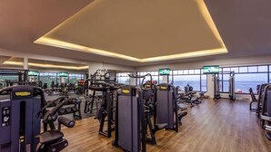 Une salle de sport équipée de divers appareils d’exercice, dotée de grandes fenêtres et offrant une vue sur l’océan.