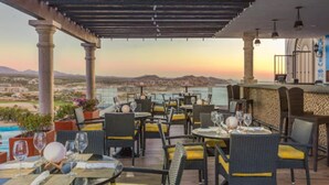 Un espace de restauration en plein air, avec des tables et des chaises, offrant une vue panoramique sur la mer et les montagnes lointaines.