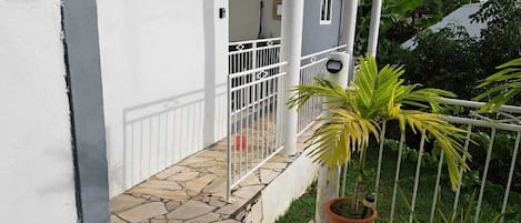 Enjoy a peaceful outdoor space with a covered patio, potted plant, and balcony overlooking lush greenery.