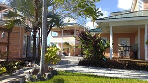 A courtyard with a paved walkway, palm trees, and a building with a covered patio area. - Tallis Palace. 1-bedroom apartment with WiFi, AC in sunny Freeport. Car offered. (Freeport)
