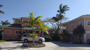 A residential area with a white SUV parked in a driveway, surrounded by palm trees and a two-story house with a green roof. - Tallis Palace. 1-bedroom apartment with WiFi, AC in sunny Freeport. Car offered. (Freeport)