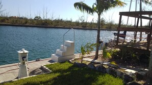 A waterfront area with a concrete staircase leading to a dock, surrounded by grass and palm trees. - Tallis Palace. 1-bedroom apartment with WiFi, AC in sunny Freeport. Car offered. (Freeport)