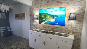 Un salon moderne doté d’un grand téléviseur à écran plat fixé sur un mur à texture, d’un meuble de rangement blanc en dessous et d’un tapis à motifs.