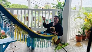 Une personne se détend dans un hamac, sous une terrasse couverte, entourée de plantes en pot et bénéficiant d’une vue sur les environs.