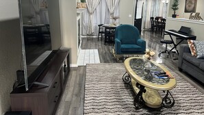 Un saló modern amb un televisor de pantalla plana, un butac armchair de color turquesa, una taula de cafè de vidre i un sofà gris.