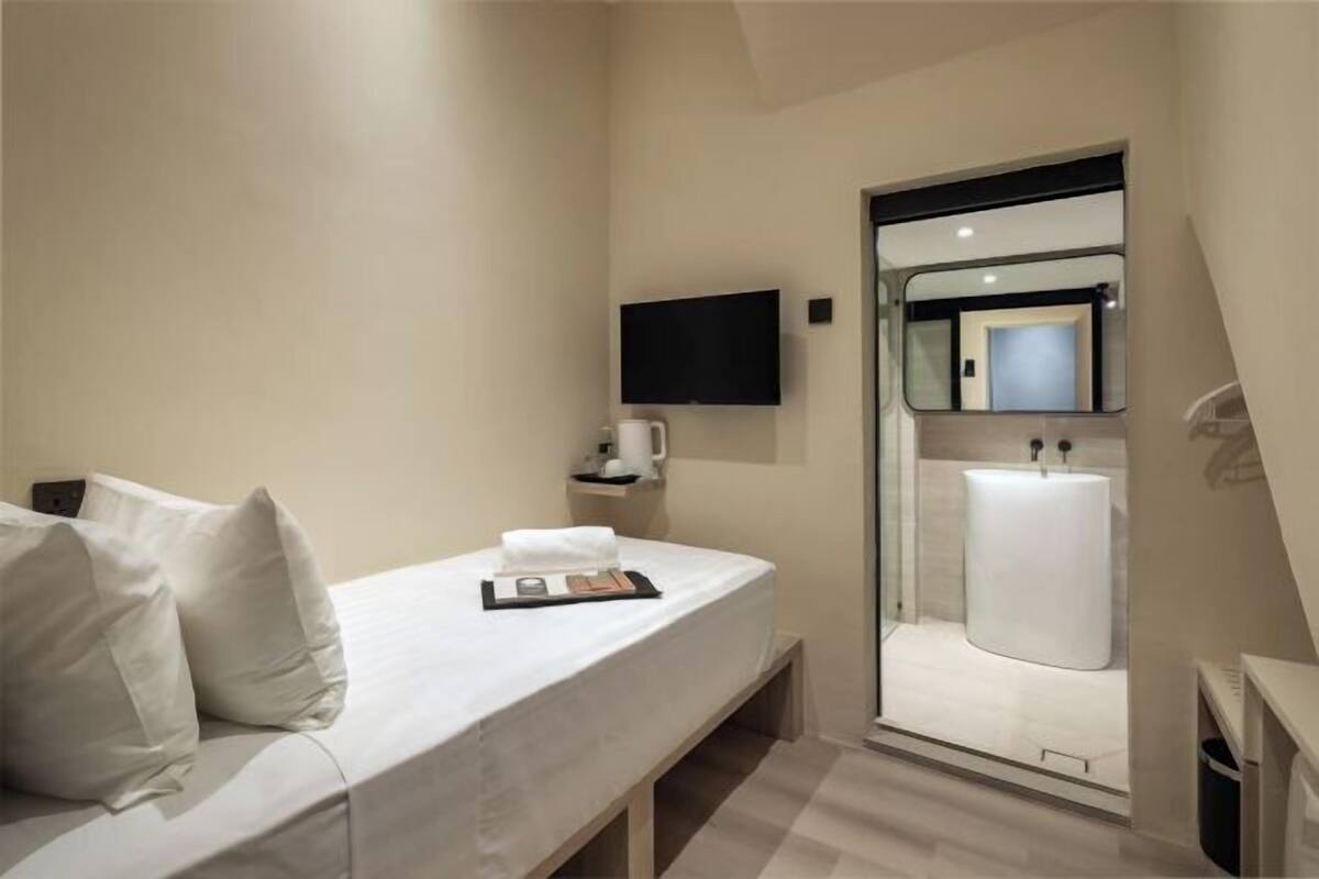Une chambre d’hôtel équipée d’un lit, d’un téléviseur à écran plat, d’un miroir et d’une salle de bain visible à travers une porte en verre.