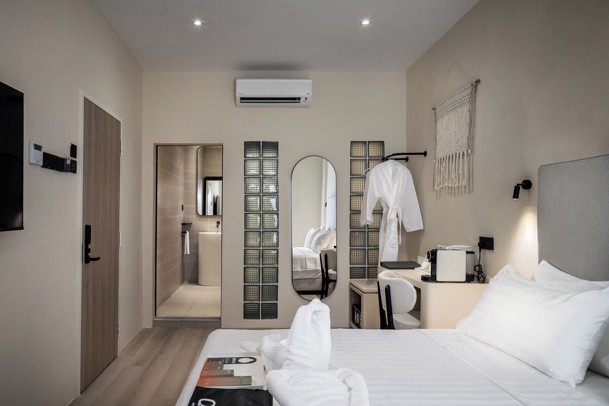A modern hotel room with a large bed, a bedside table with a lamp, a mirror, and a wall-mounted air conditioner.