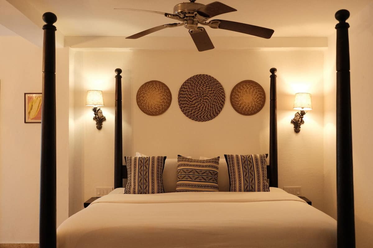 A four-poster bed with patterned pillows, wall sconces, and decorative wall art.