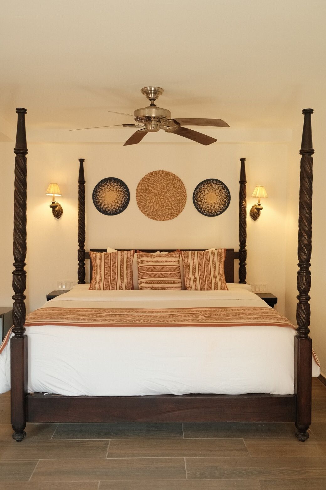 A four-poster bed with a ceiling fan, wall sconces, and decorative plates.