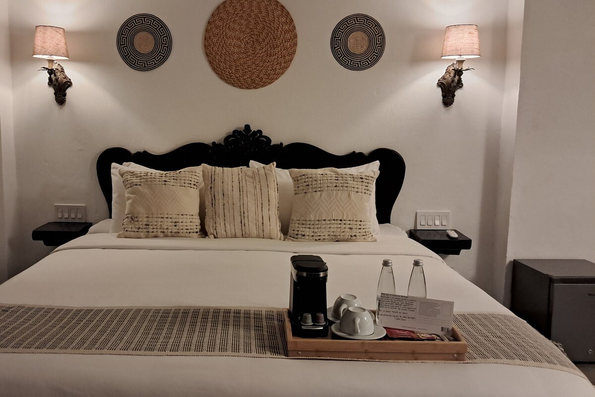 A neatly made bed with a headboard, two wall-mounted lamps, and a tray with a coffee pot, cups, and a menu on the bedside table.