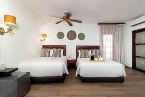 A hotel room with two beds, a ceiling fan, wall sconces, a minibar, and a large window with curtains. - Hotel Boutique Patio Corao By GEH Suites (Cartagena)