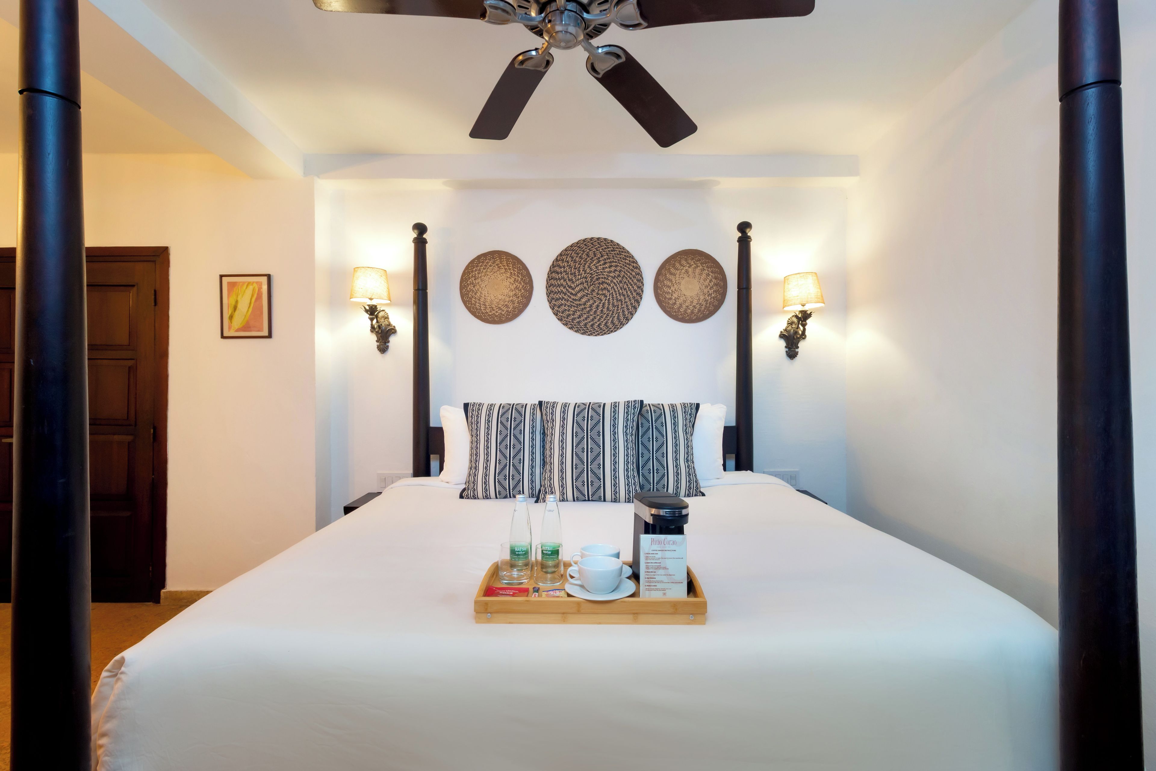 A hotel room with a large bed, a ceiling fan, wall sconces, and a tray with breakfast items.