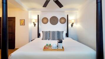 A hotel room with a large bed, a ceiling fan, wall sconces, and a tray with breakfast items.