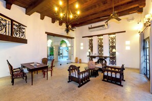 A spacious room with a high ceiling, a chandelier, a ceiling fan, and a large window with curtains. - Hotel Boutique Patio Corao By GEH Suites (Cartagena)