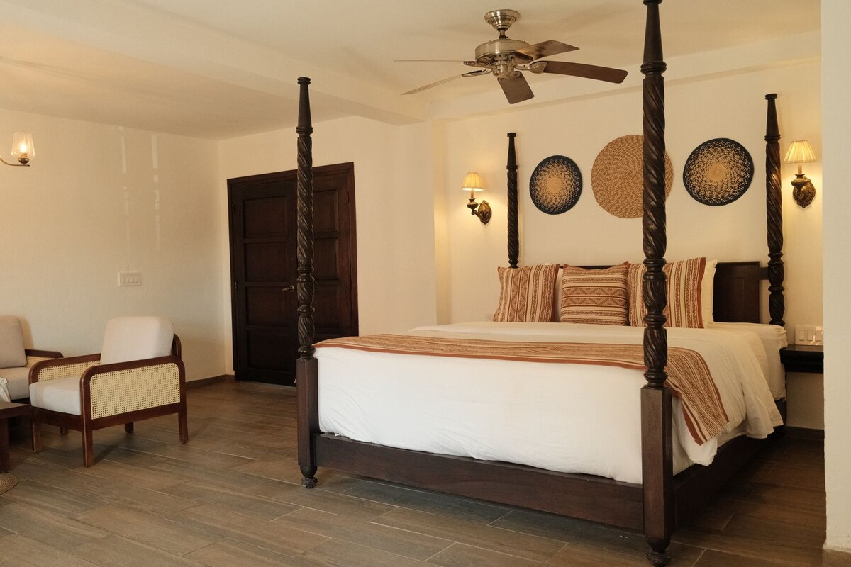 A four-poster bed with a ceiling fan, a wooden door, and wall-mounted lamps.