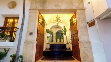 Uma entrada imponente com um arco de pedra, uma escadaria que leva a um andar superior e uma câmera de segurança na parede.