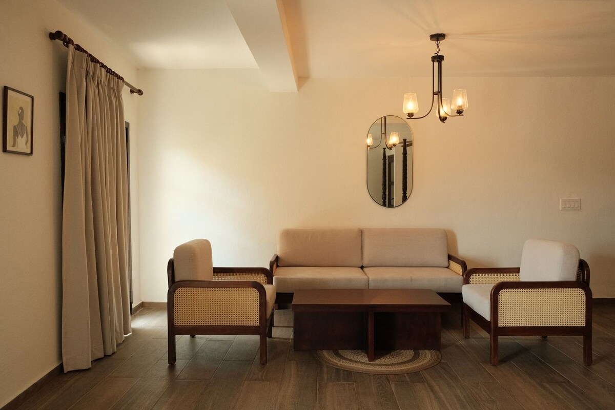 A living room with a sofa, two armchairs, a coffee table, a chandelier, and a mirror on the wall.